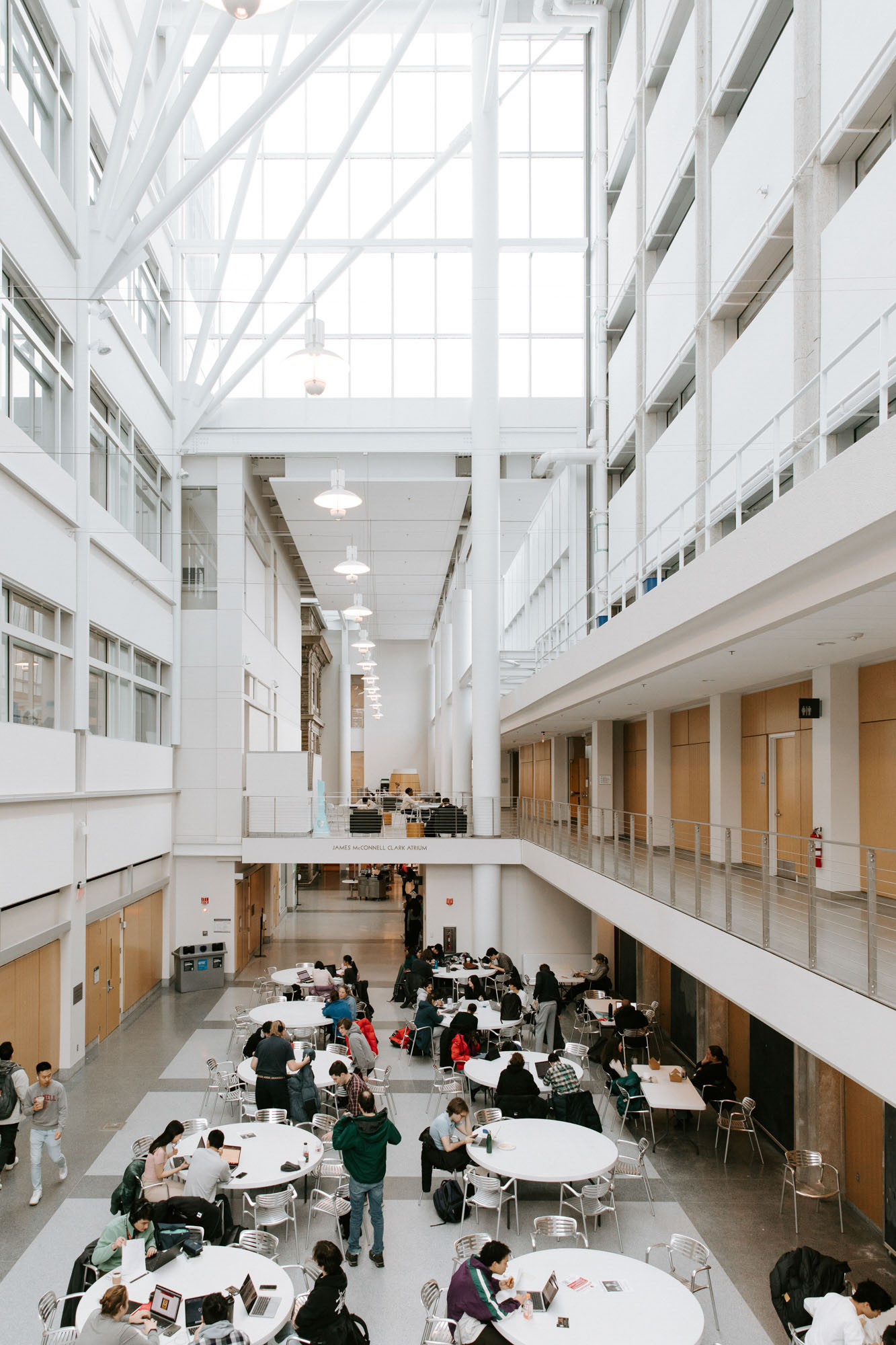 Vertical view of Clark atrium showing high ceilings, Clark Hall balcony, and several tables with students seated around them.