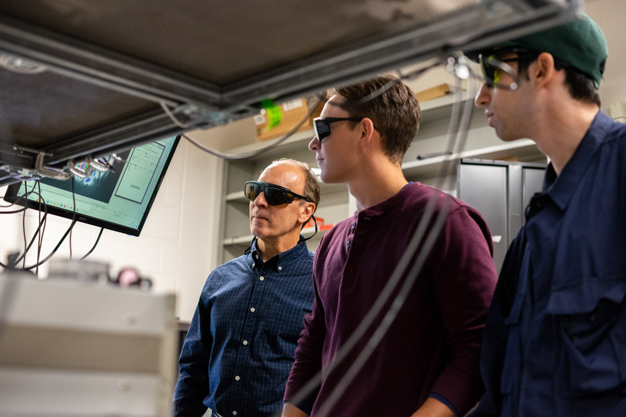 Frank Wise, Henry Haig, and Yishai Eisenberg look at something outside the photo frame in the Wise Lab.