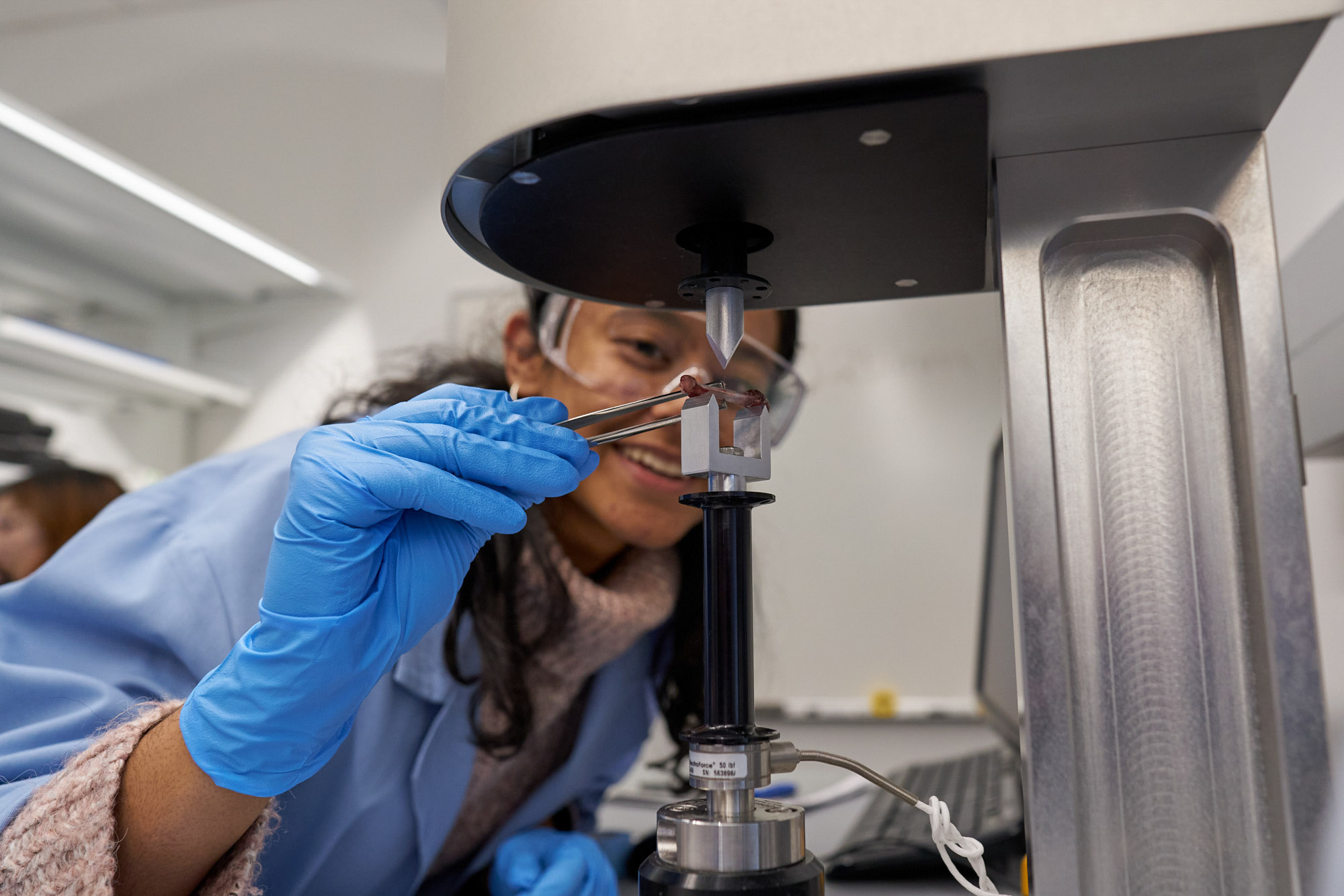 A student wearing a blue lab coat and blue gloves conducts an experiment in professor Lawrence Bonassar's class.