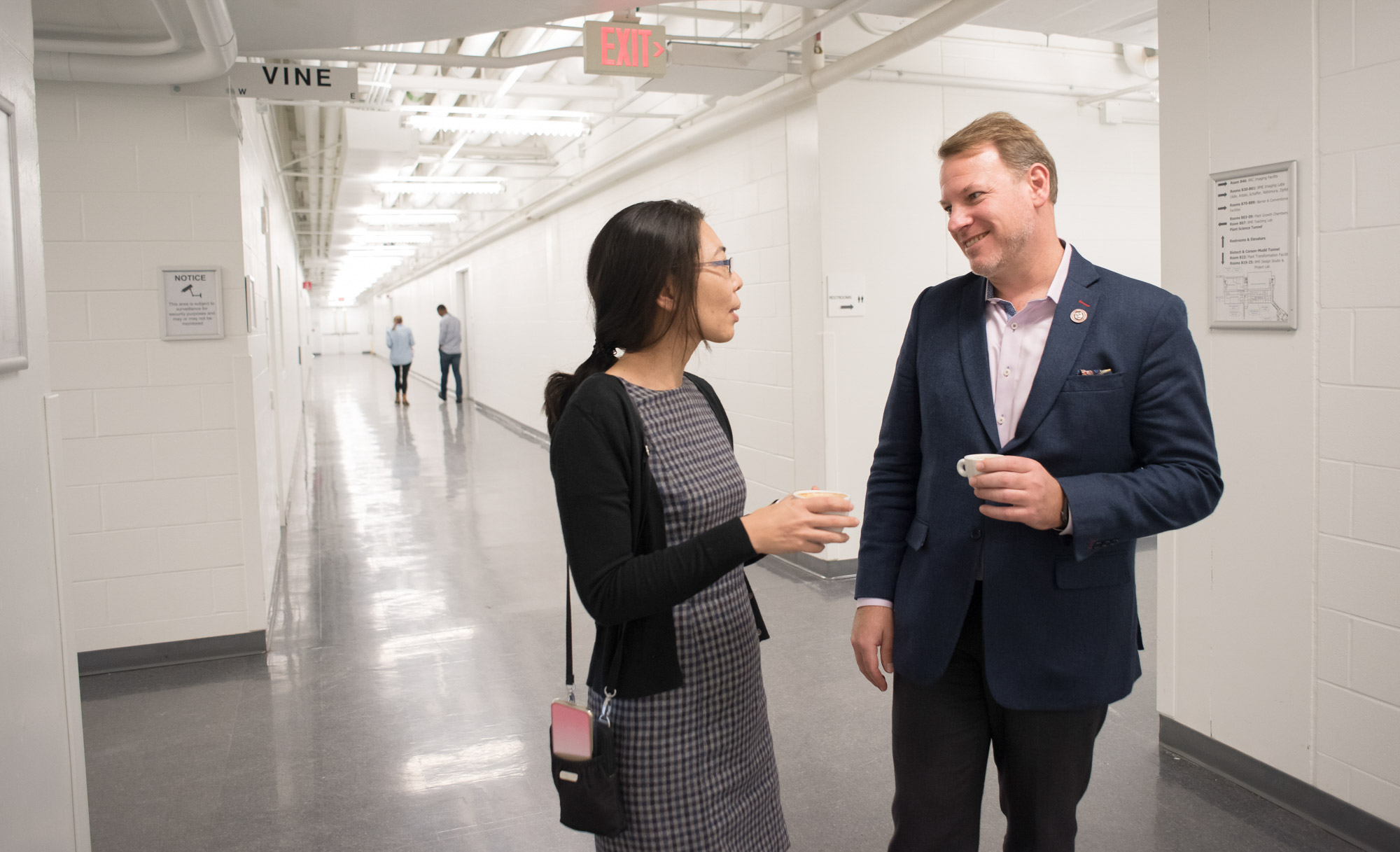 Professors Nozomi Nishimura and Chris Schaffer hold coffee cups while talking in the hallway outside the Schaffer-Nishimura lab.