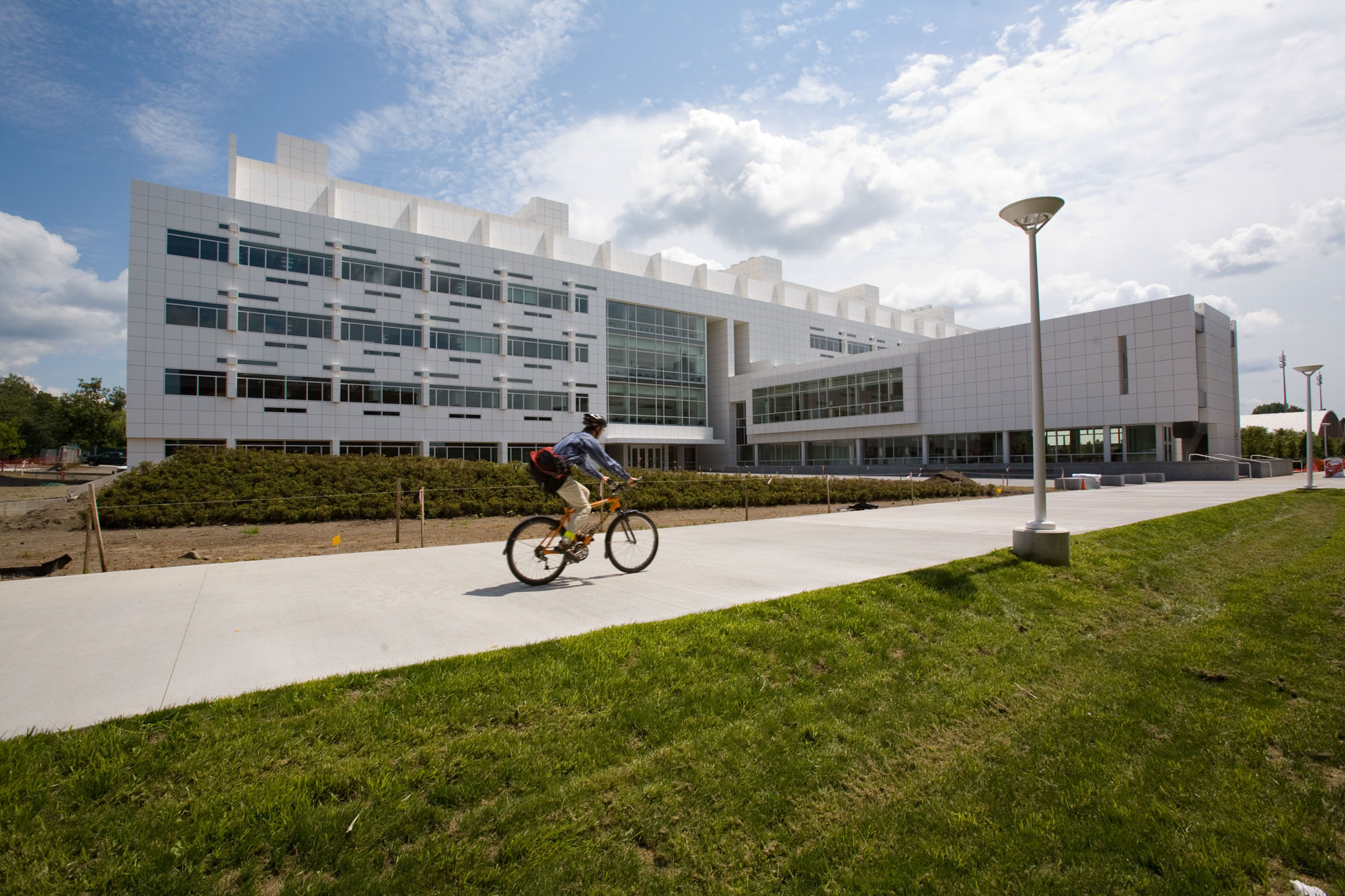 A student rides their bike past Weill Hall - home of the Meinig School of Biomedical Engineering - on a mostly sunny summer day.
