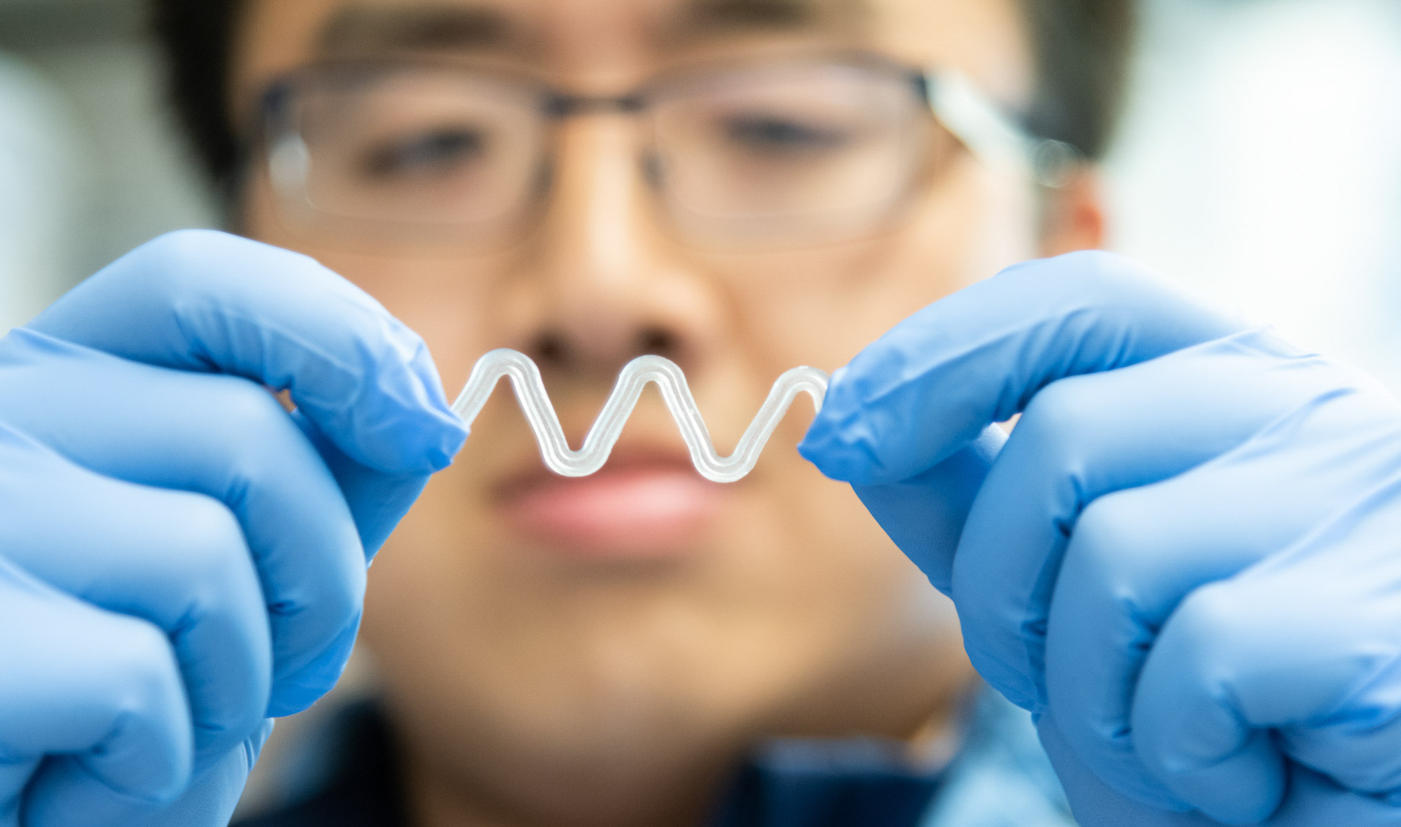 A student wearing a blue lab coat and blue gloves holds an experiment in the Yadong Wang lab