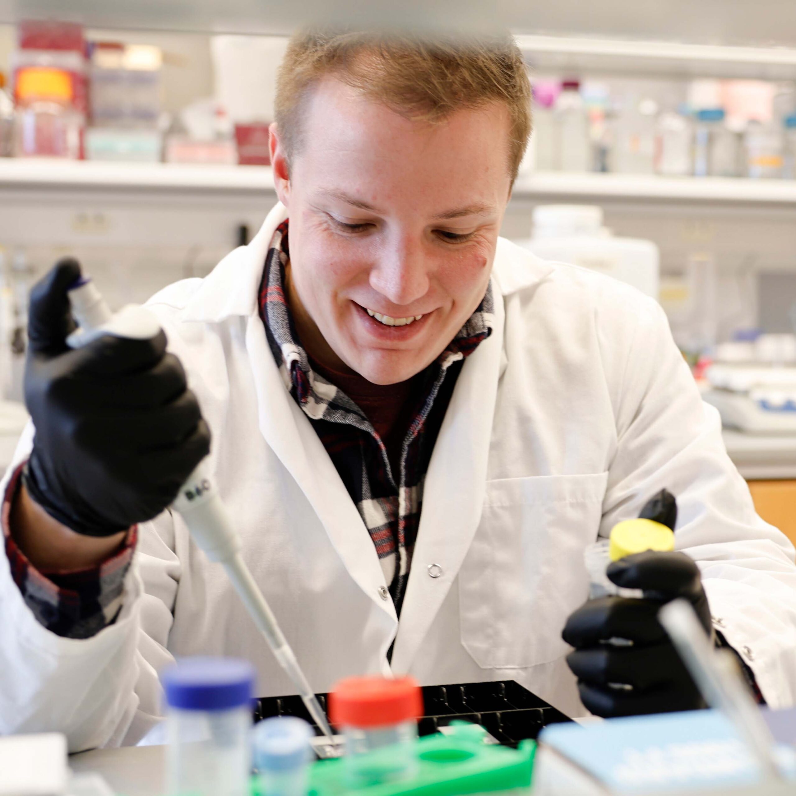 A PhD student wearing a white lab coat and protective gloves conducts an experiment in a BME lab