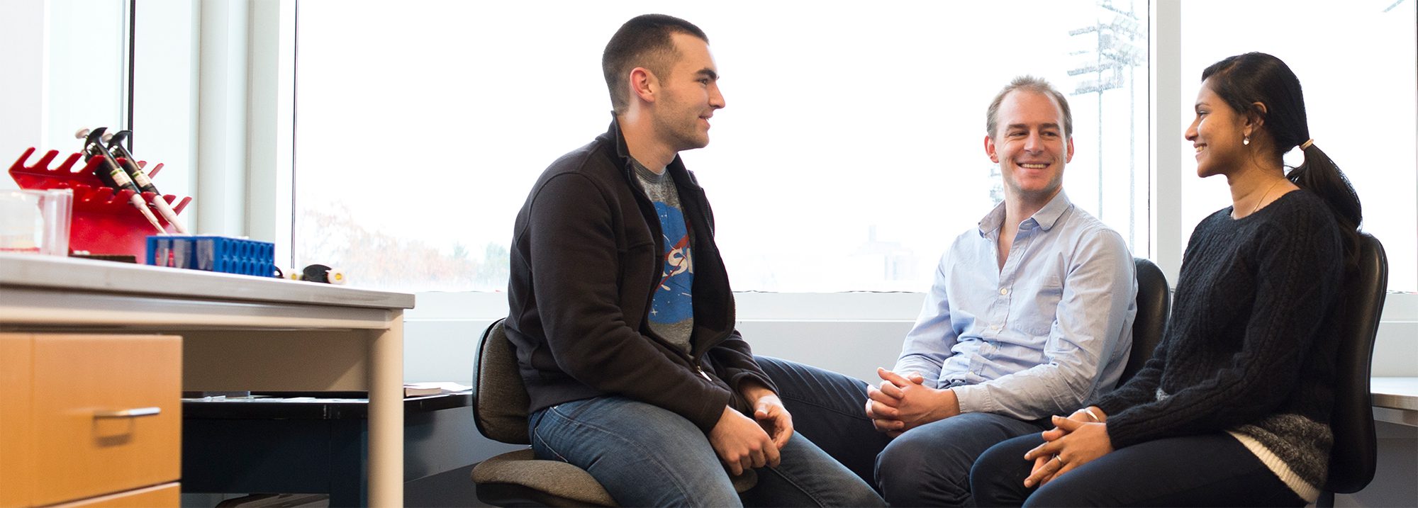 Professor Iwijn De Vlaminck sits with students in laboratory.