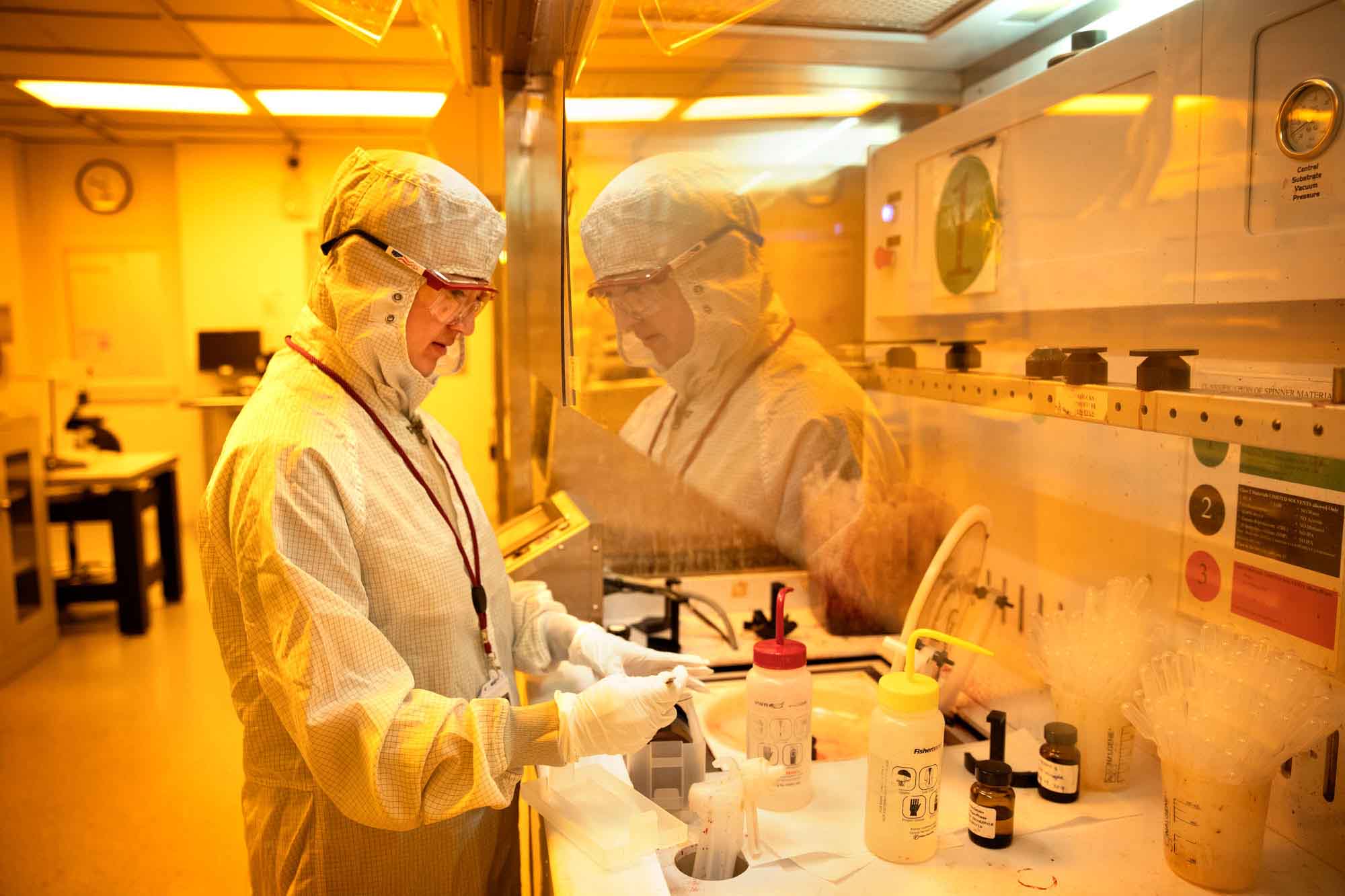 Person wearing clean room suit works at a fume hood at Cornell Nanoscale Facility.