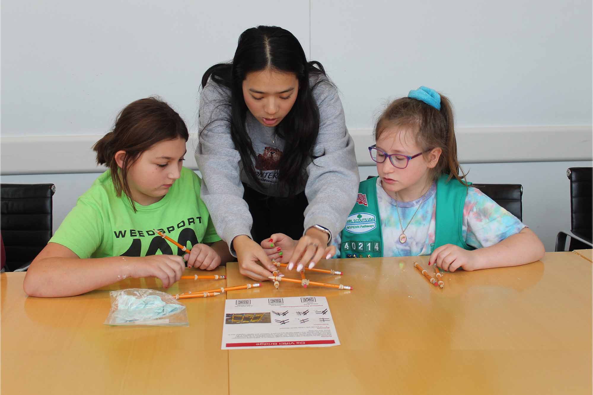 Graduate student works at a table with two girl scouts on a biomedical engineering project in Weill Hall.