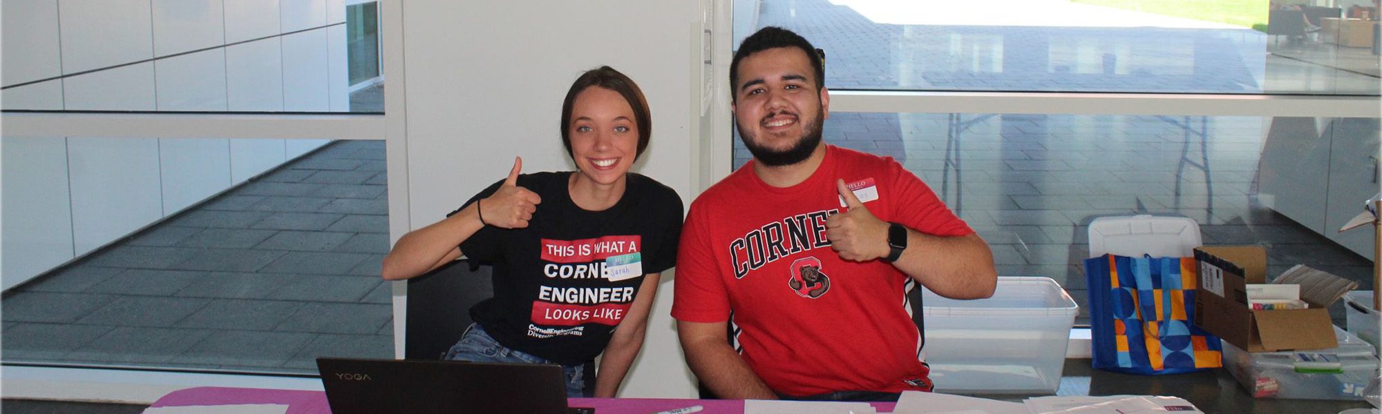 Graduate students sit at table in Weill Hall thumbs up for outreach event.