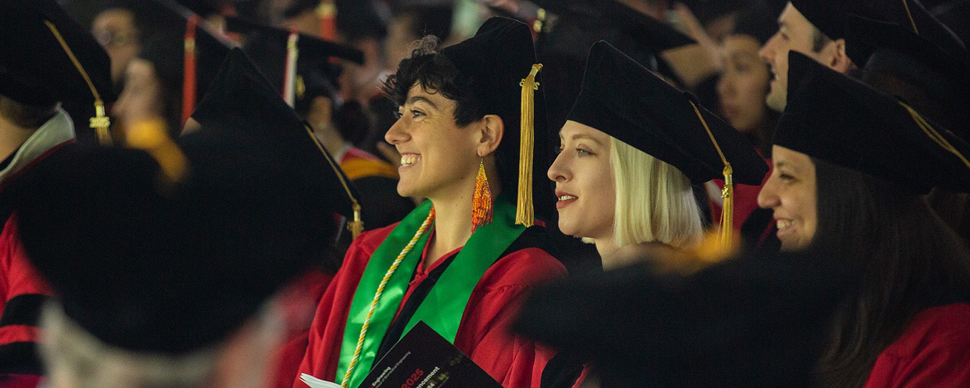 Ph.D. 2025 graduates Marguerite Pacheco and Cara Robertus sit in regalia at the commencement ceremony.