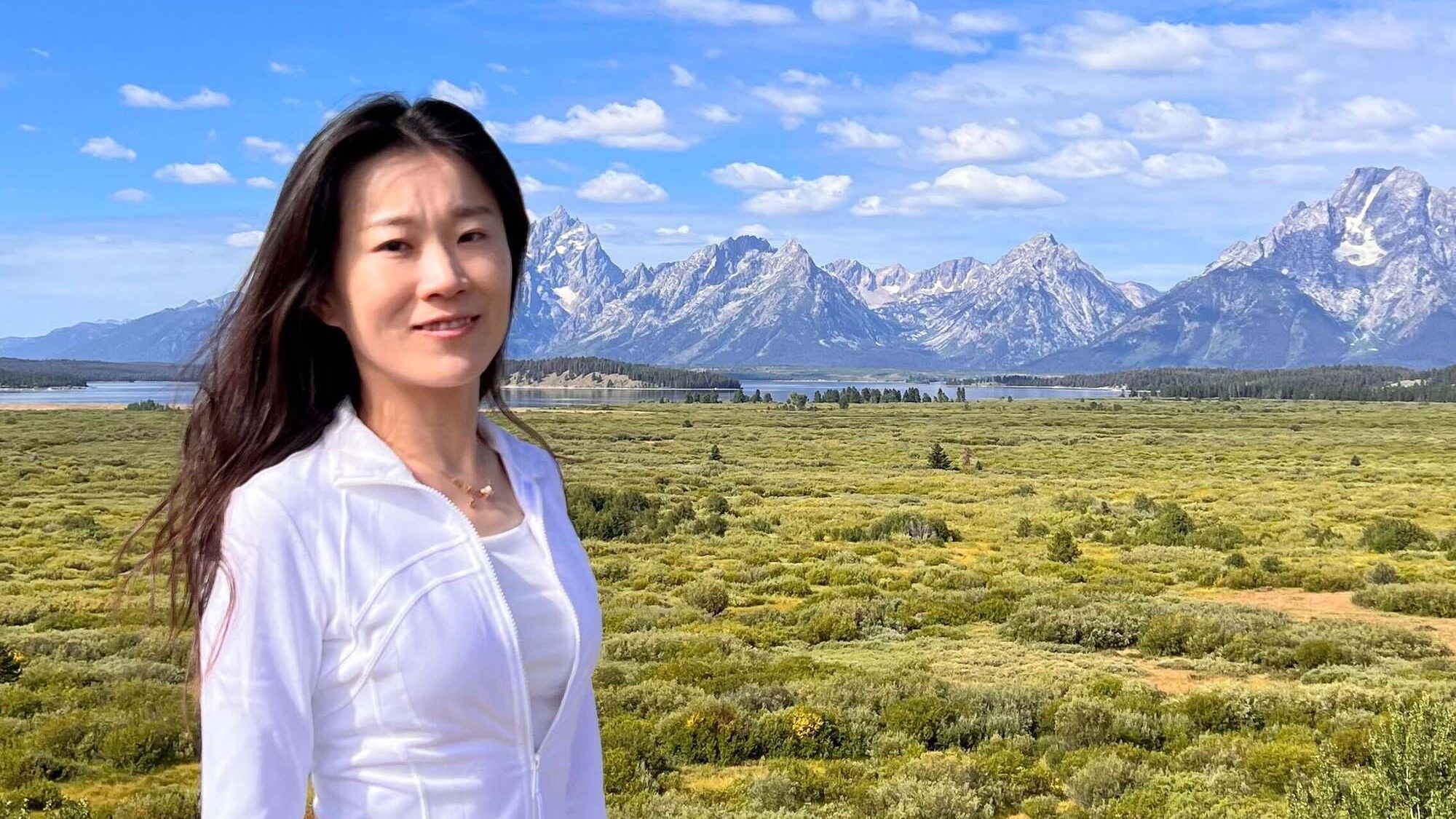 Kwan lab postdoc Lingxiao Shao stands outdoors with mountains behind her.