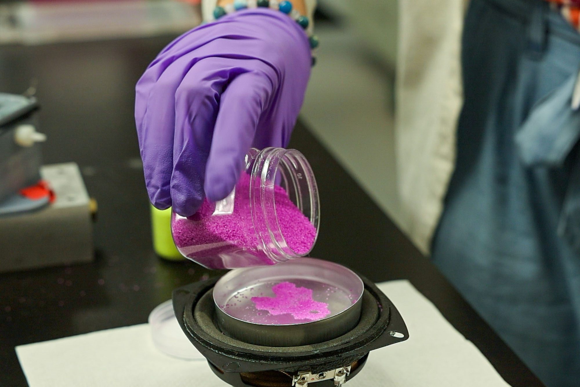 Gloved hand pours particles into liquid filled dish in the Tobias Hanrath lab.