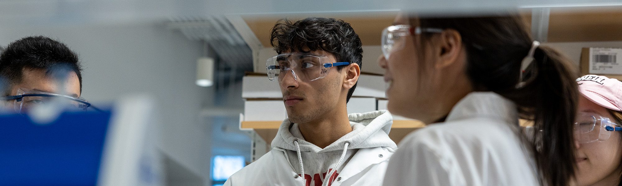 Students and faculty in safety glasses, lab coats work together in Olin Hall lab.