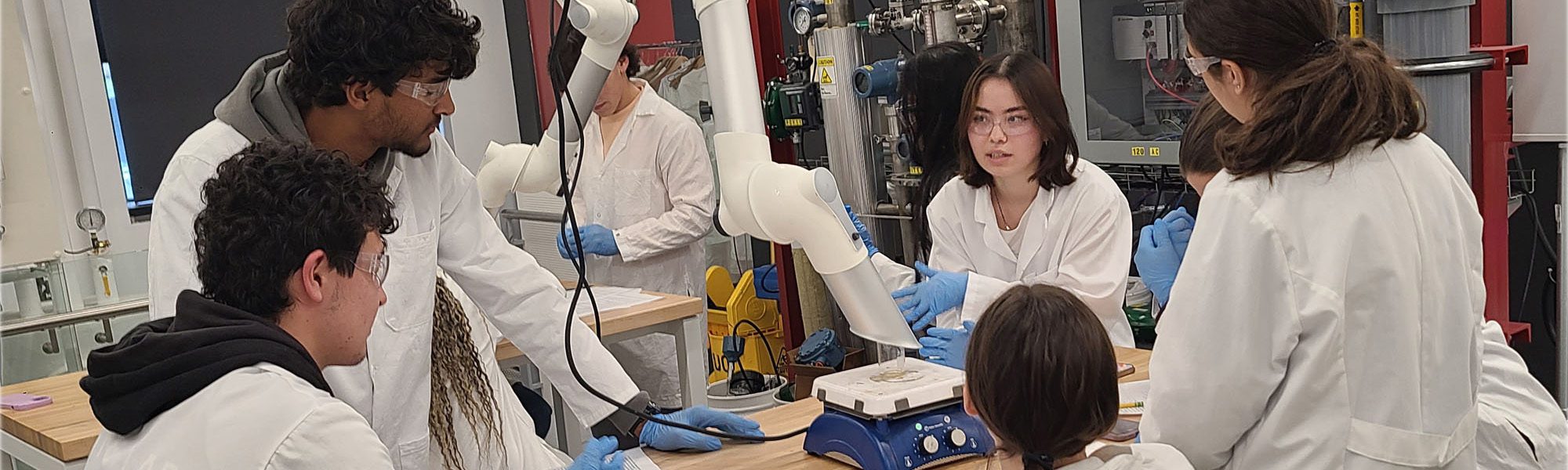 Undergraduate students in active learning initiative ALI stand in lab coats with equipment.