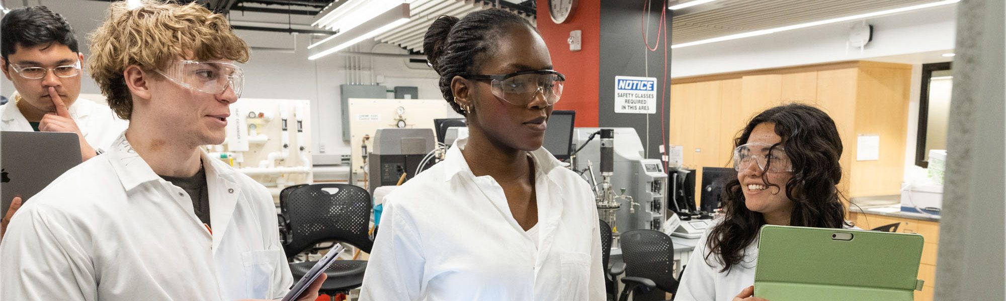 Undergraduate students wearing lab coats work with computers in the Olin Hall Unit Operations Lab.