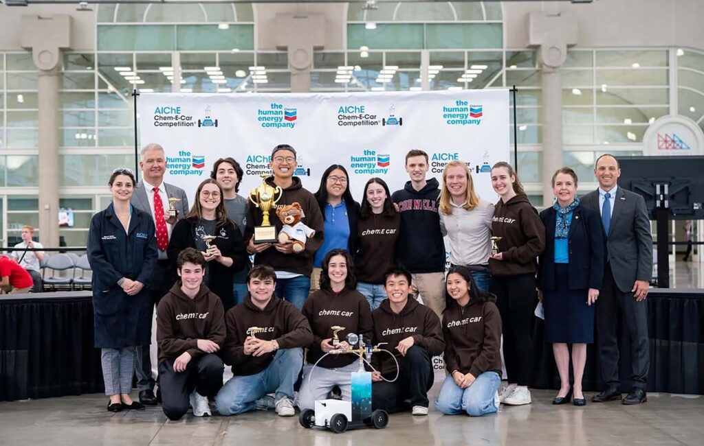The ChemE car team of undergraduates stand together with competition leadership.