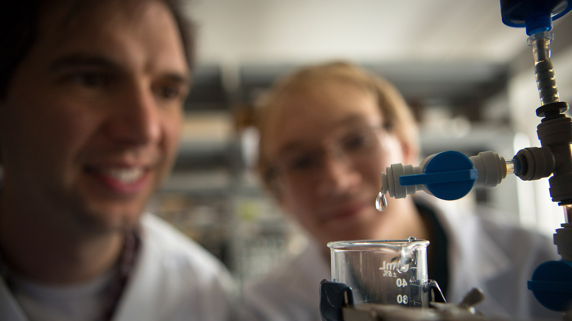Damian Helbling and student watch water with micropollutants drip into a beaker in a lab
