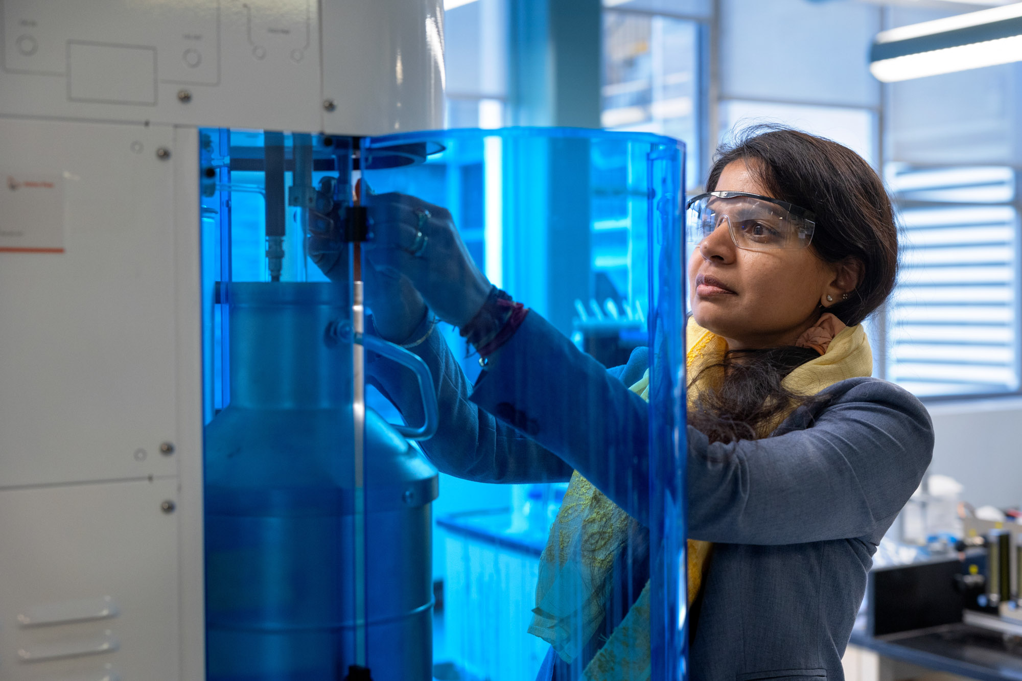 Greeshma Gadikota wearing safety glasses while operating a machine in a lab.