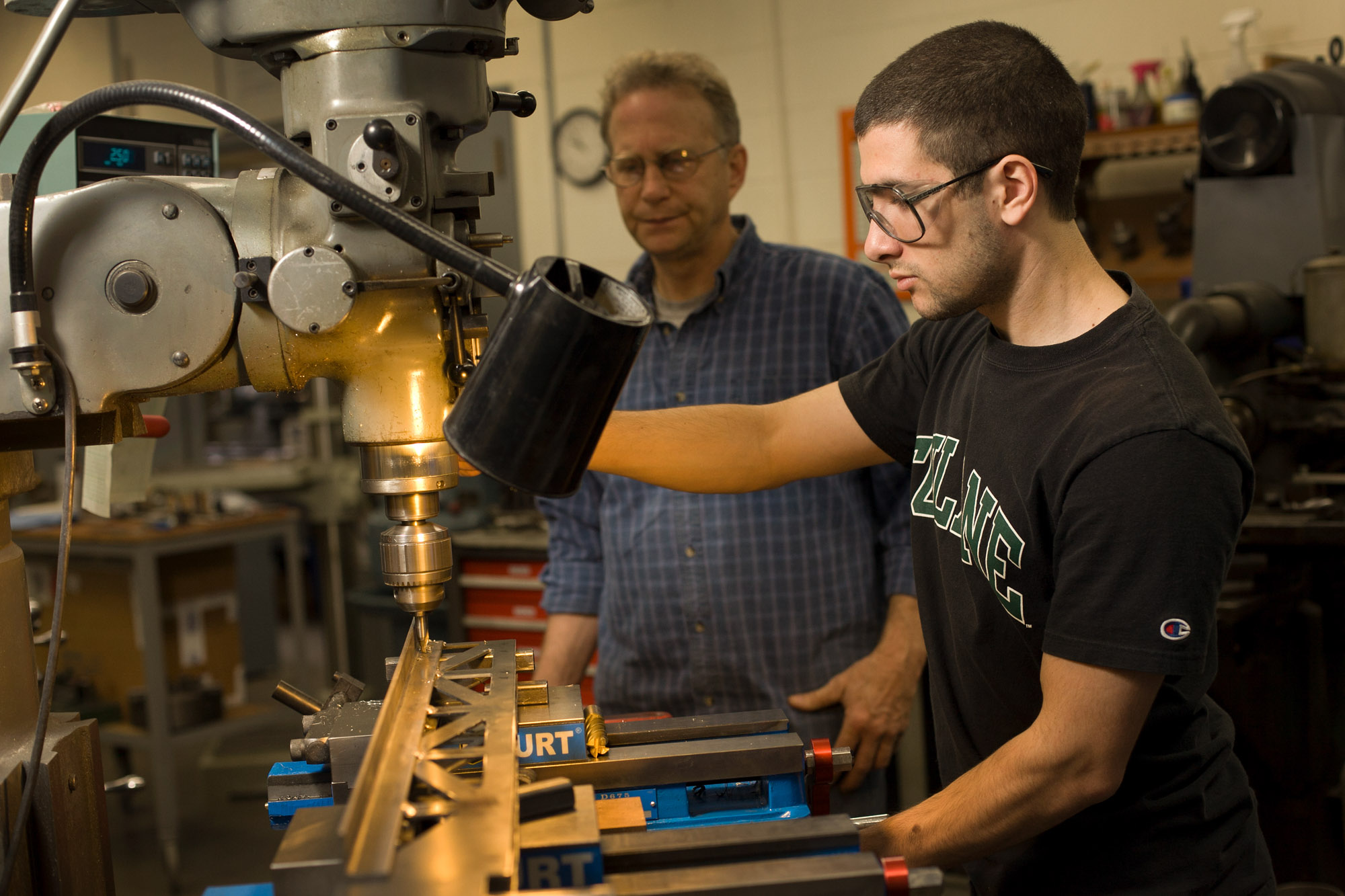 Equipment Technician Timothy Brock supervising a student using a drill press in a Civil and Environmental Engineering lab.