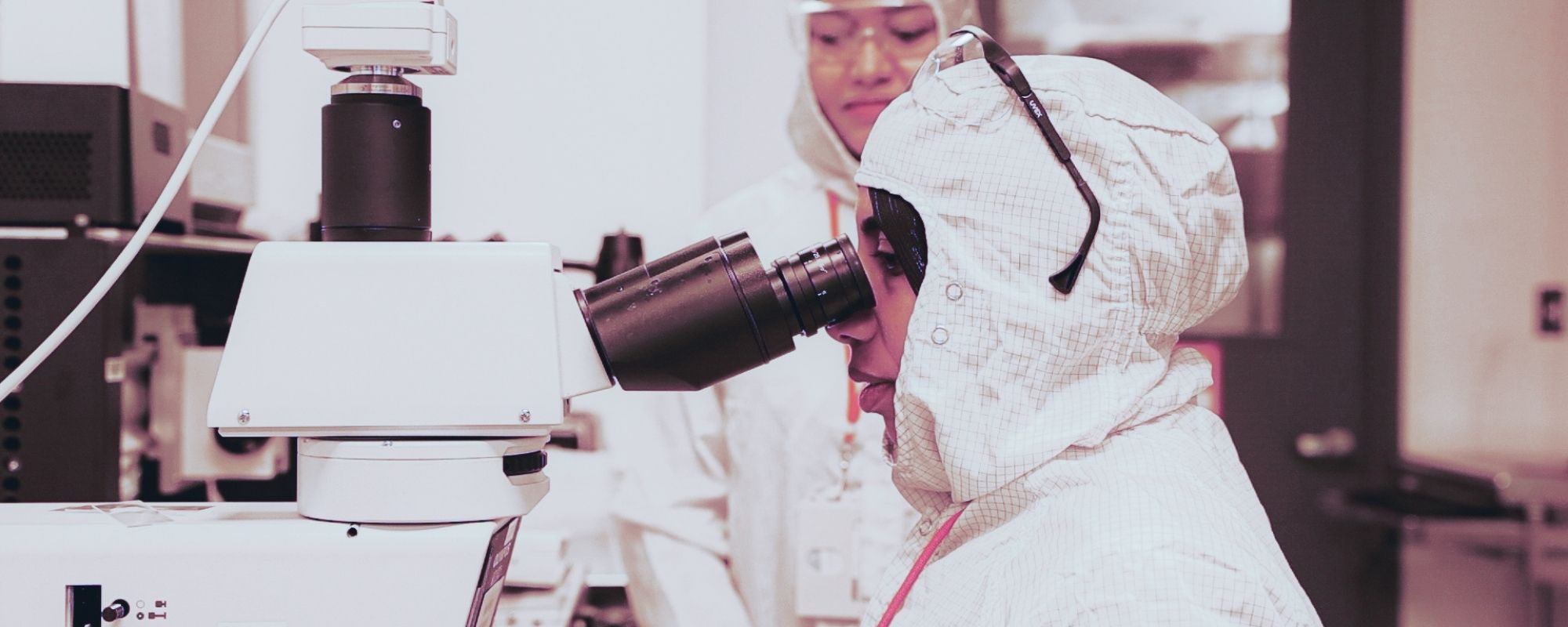 Amal El-Ghazaly wearing a full body suit in a lab while looking through a microscope.