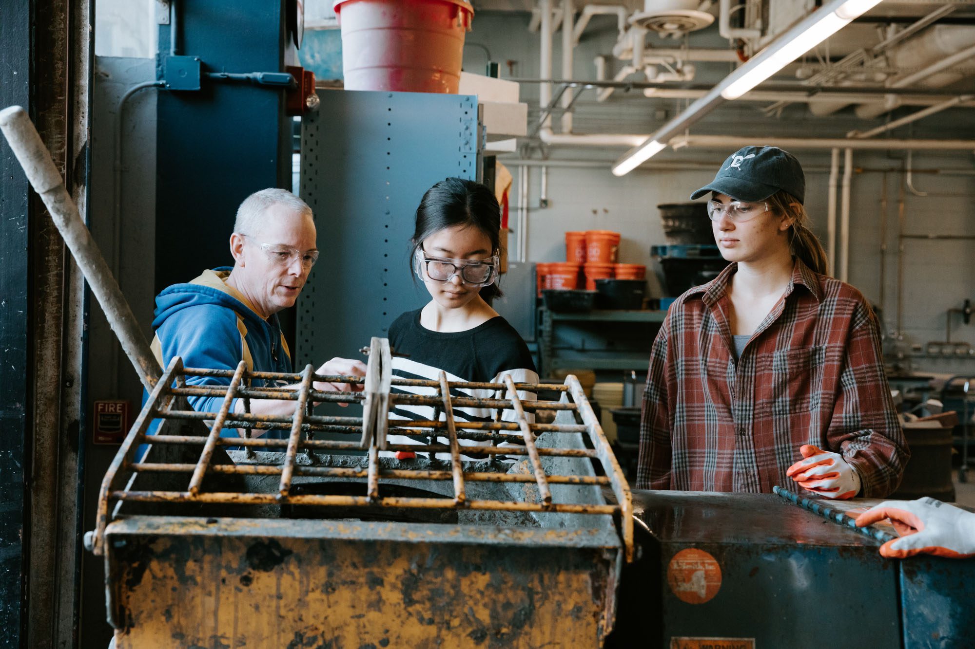 Professor Bovay works with students wearing protective glasses at large metal equipment