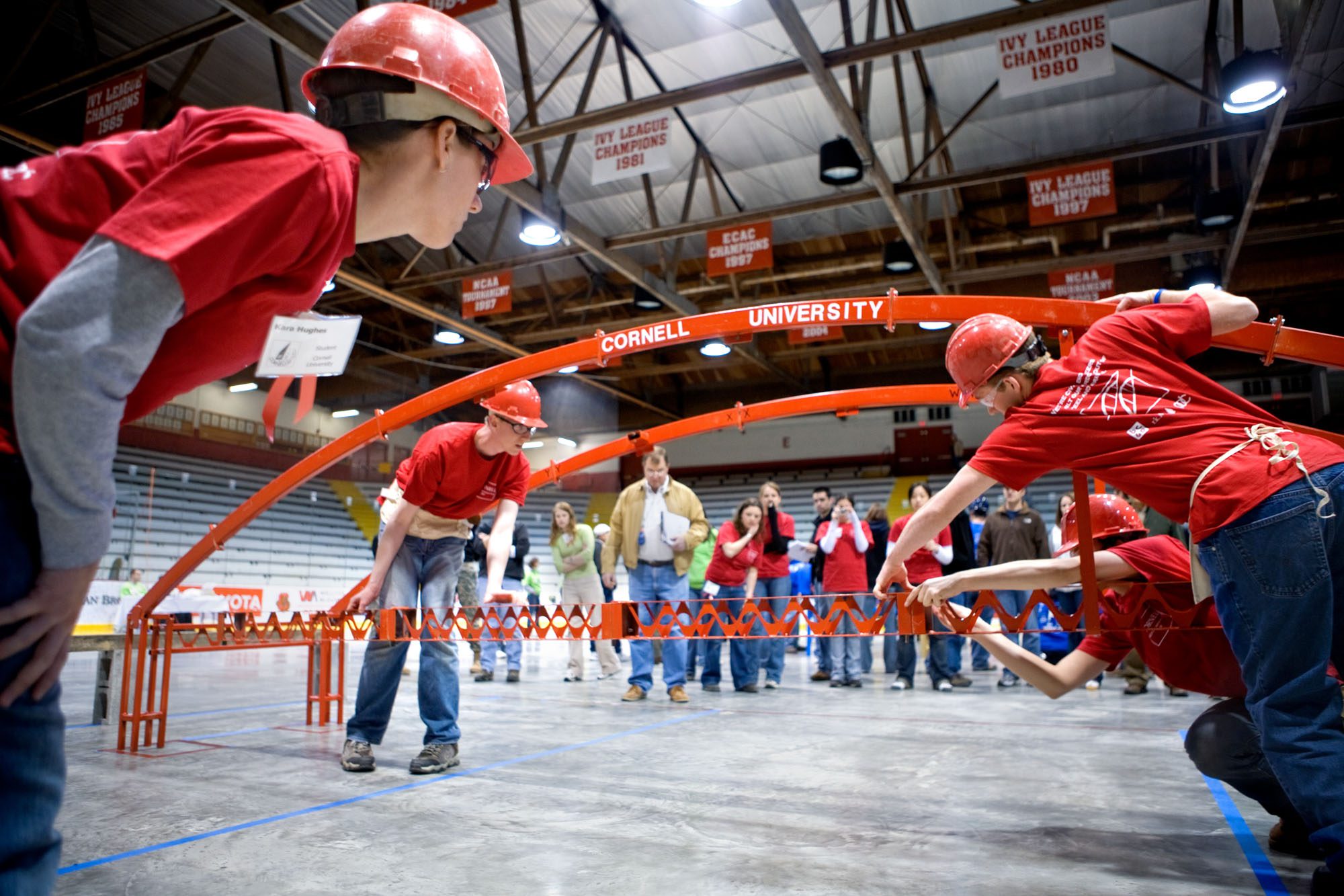 Students wearing hardhats hold bowed metal bars with Cornell University printed on one of them