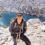 Tingan Li hiking in the mountains with a lake in the background.