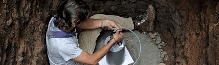 person sitting in a hole, wiring a seismic sensor.