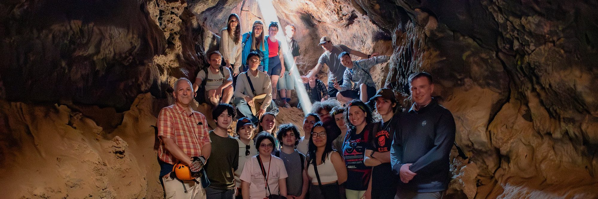 A group of people pose in a cavern with a shaft of sunlight streaming in behind them.