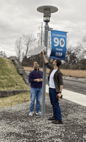 Two people look up as they attach a small solar panel and sensor to a lightpole near the Cornell campus.