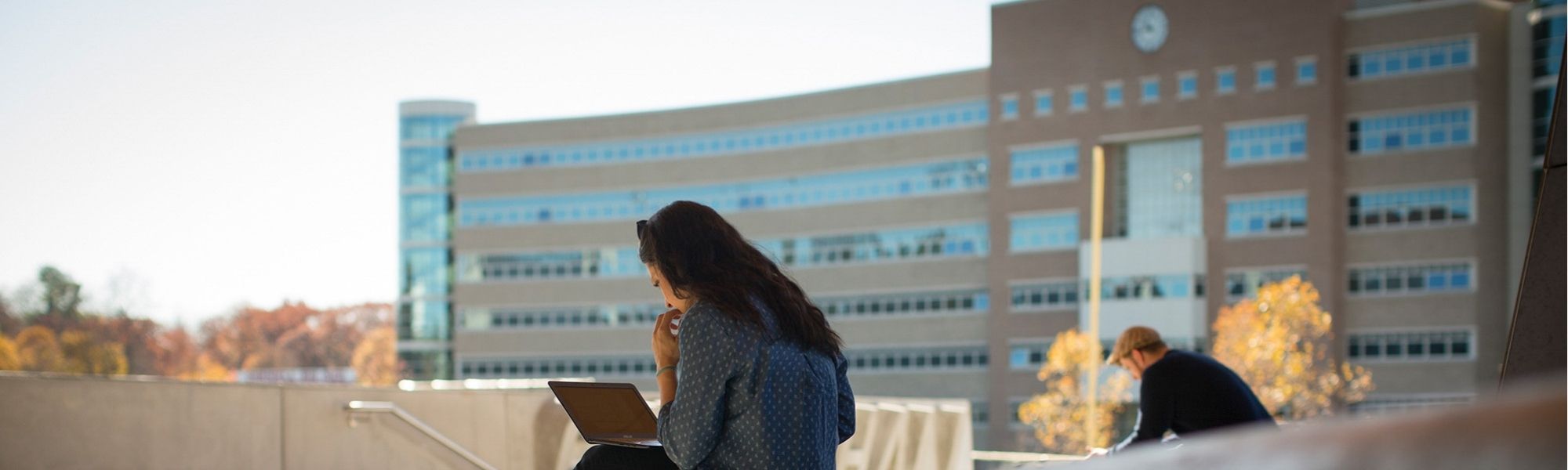 Rhodes Hall Solar Noon Clock in the background with students working on their laptops outside of Gates Hall in the foreground.