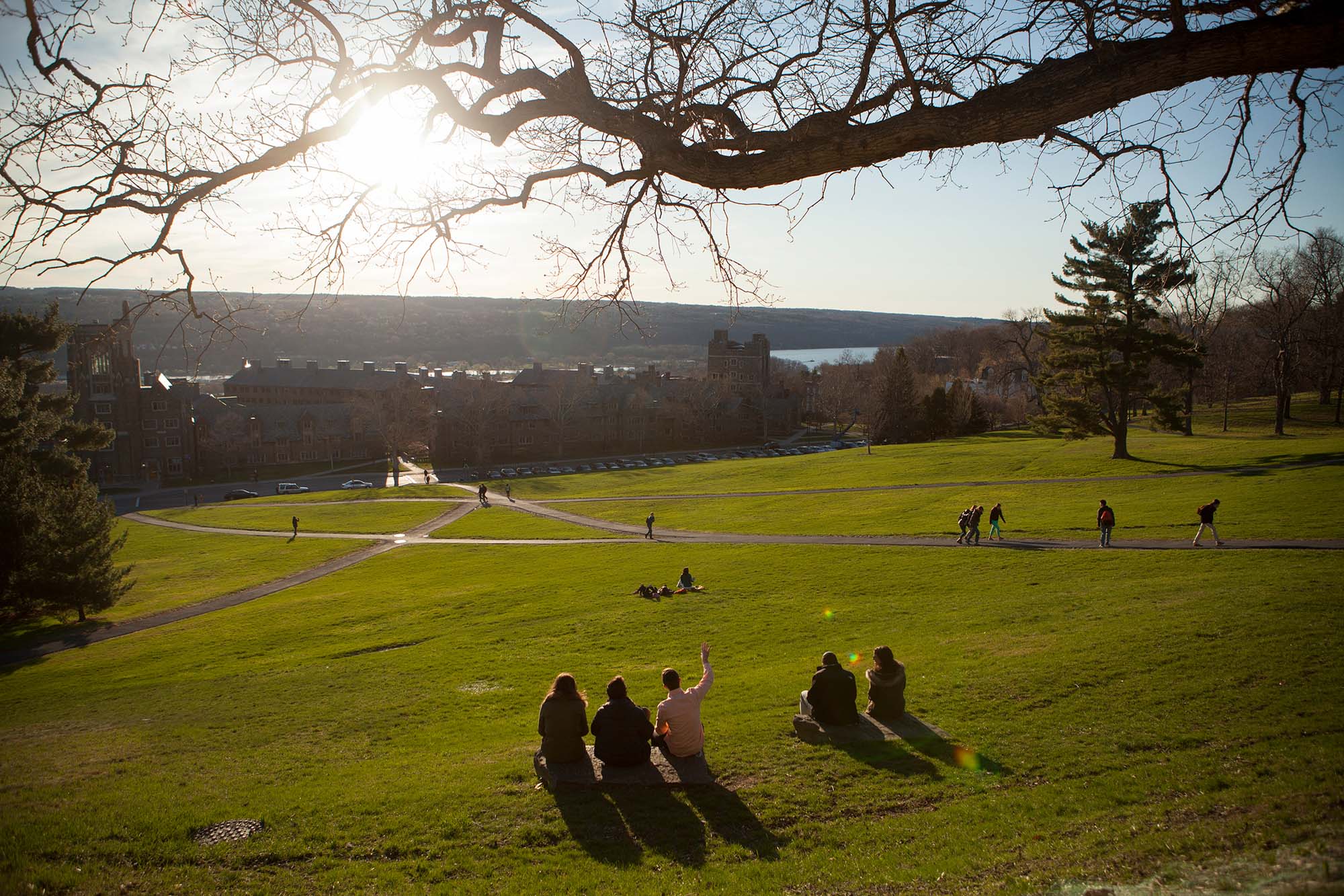 Students sit in the grass on Libe Slope as other walk to class