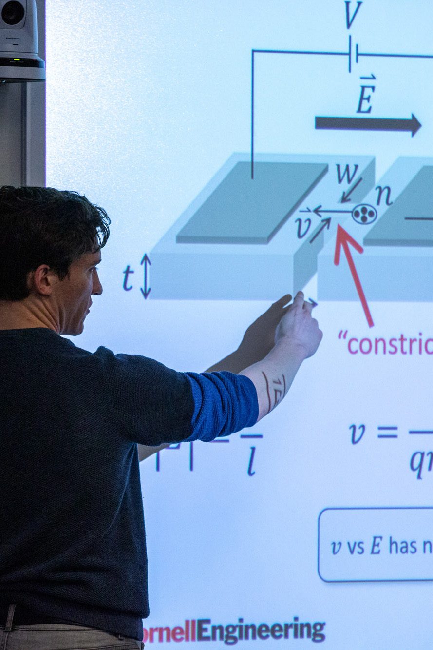 Back and profile of grad student pointing at powerpoint presentation on screen that has an equation