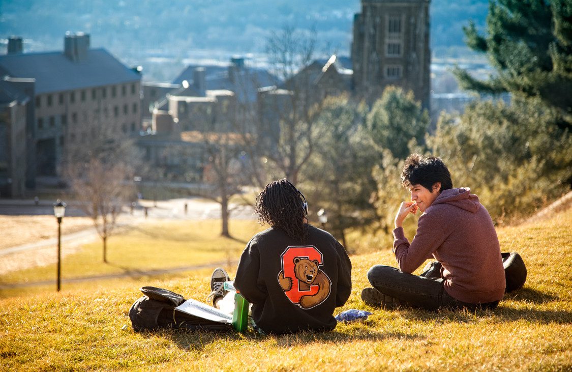 Students talk while relaxing on grassy hill