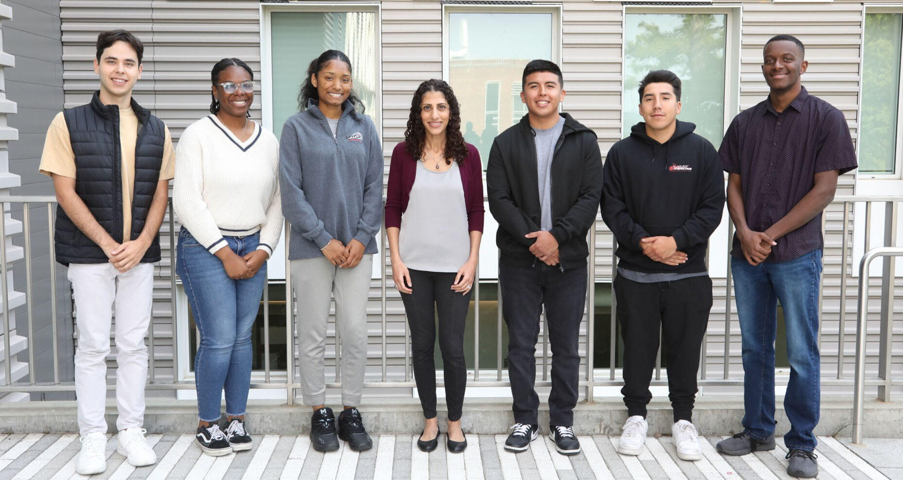 Seven people stand side-by-side in a row outside of Upson Hall. The people are Professor Nelly Andarawis-Puri and six members of the FLAME program