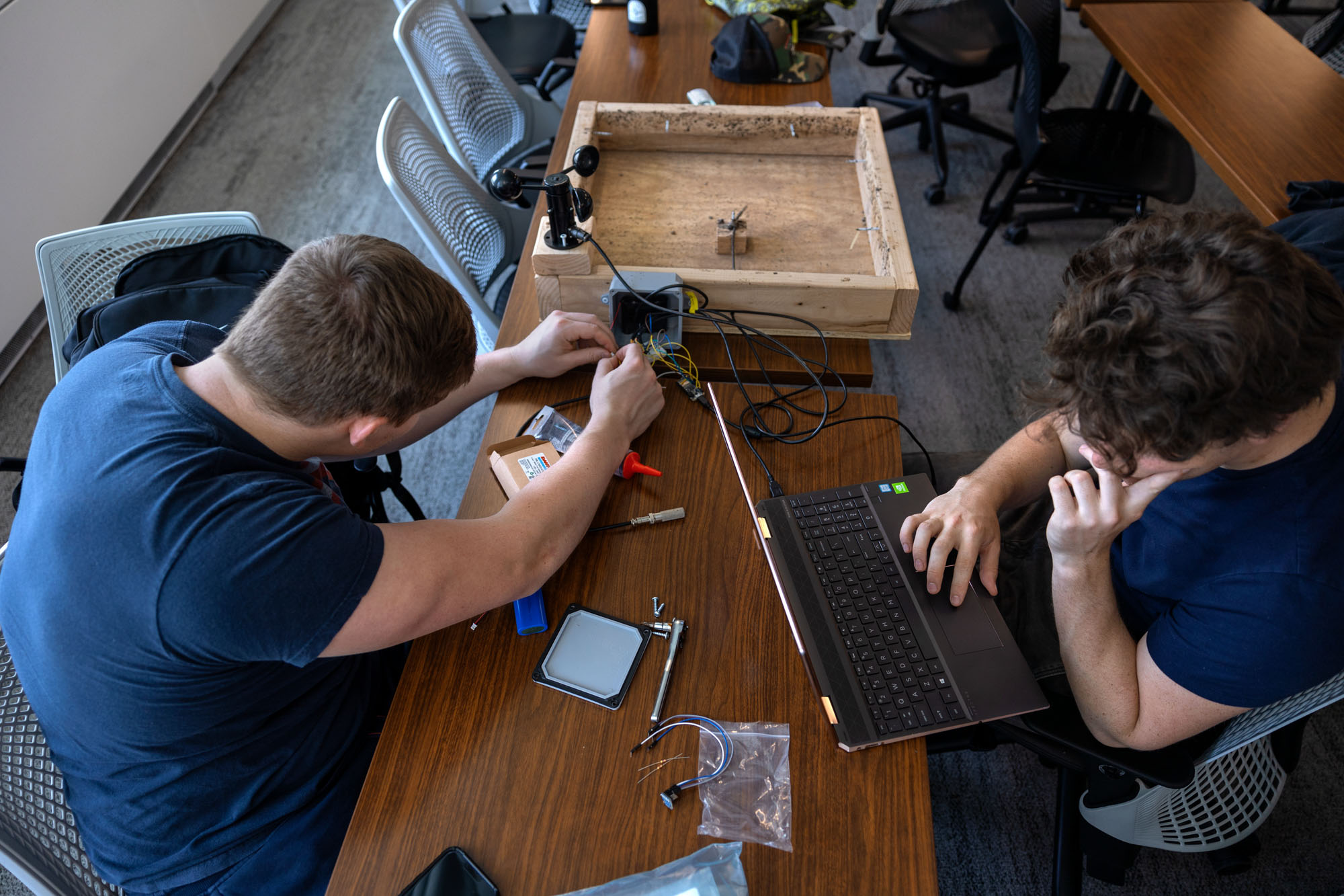 two students in blue shirts operate a laptop and electronics hooked up to a black wind vane