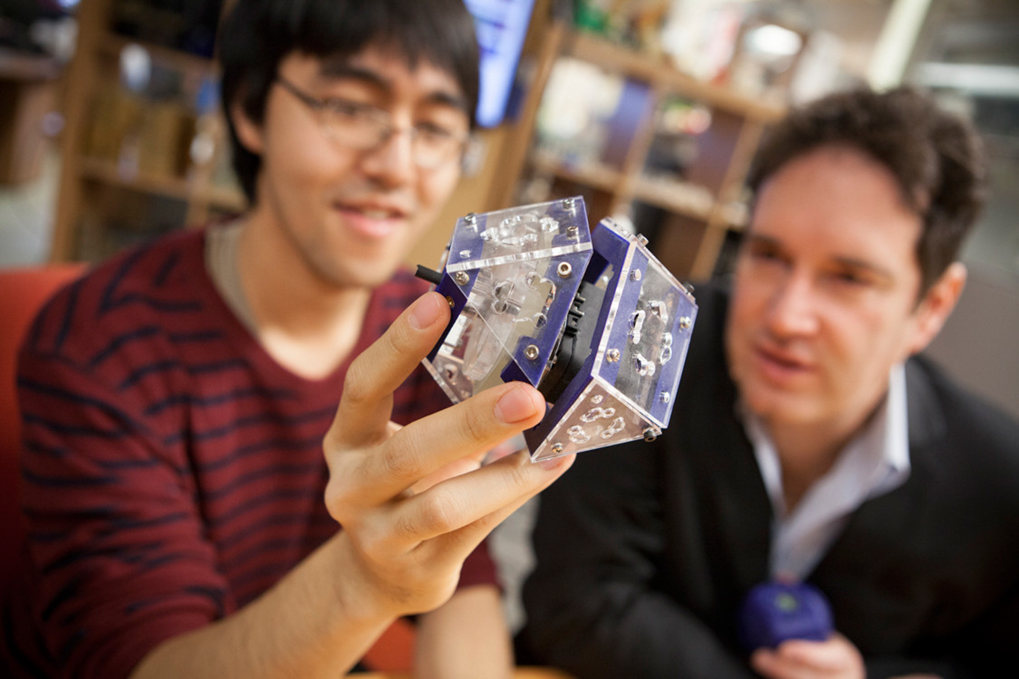 Hod Lipson works with a student in the robotics lab. The student is holding a cubic robot.