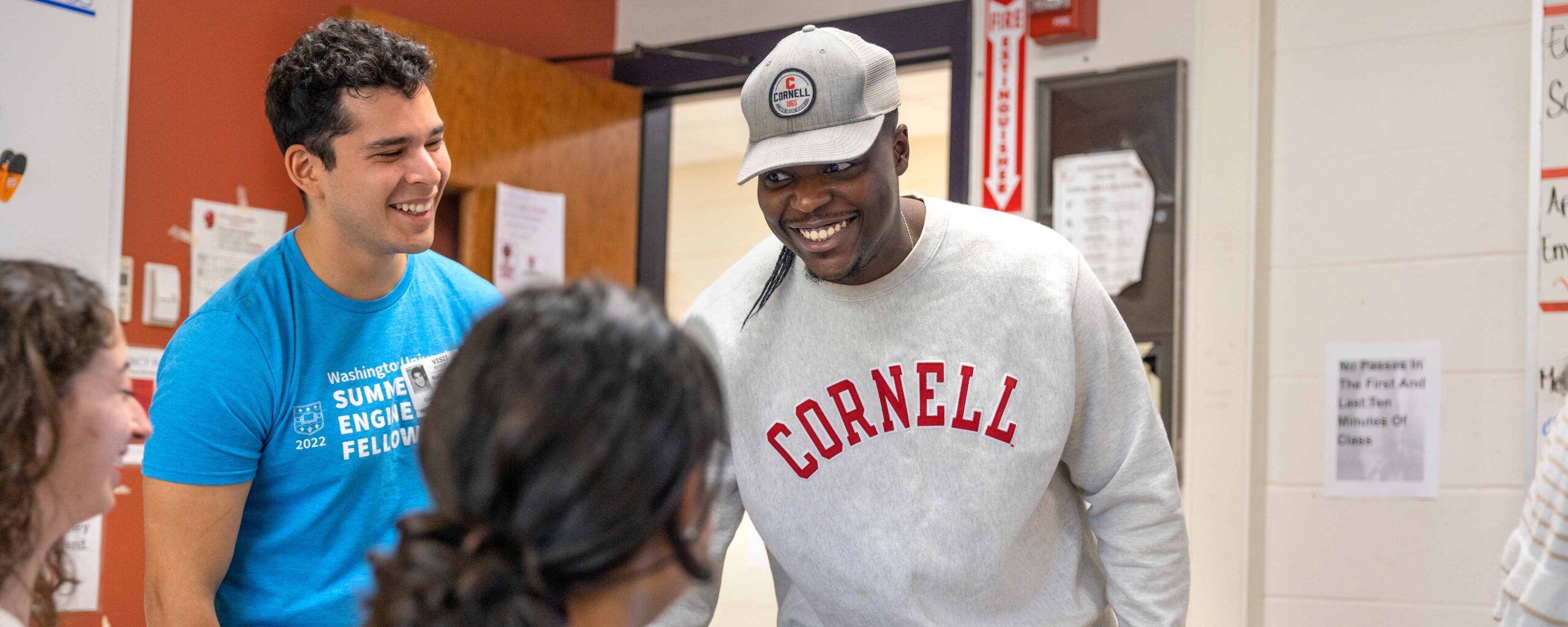 2 M.Eng. students smiling at students sitting down as part of Max Zhang Class Internet Of Things at Geneva High School