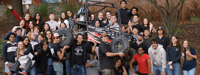 Members of the Baja Racing project team pose while holding their car off the ground.