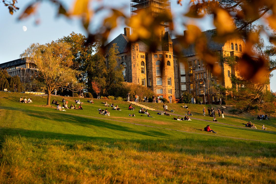 Students enjoy Libe slope during an autumn sunset, with Willard Straight, Olin, and Uris Library in the background.