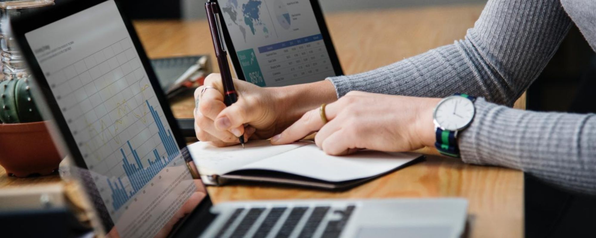 Hands writing a paper in between laptops