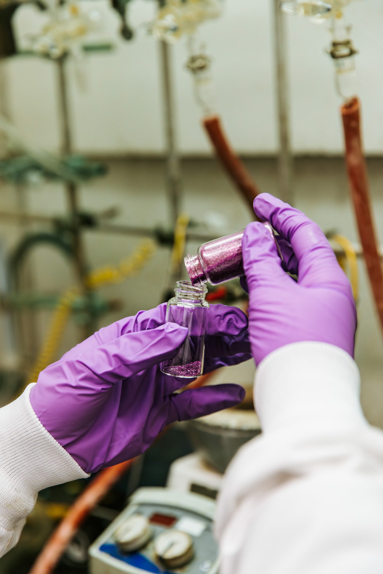 hands pour a shiny purple material from one jab into another