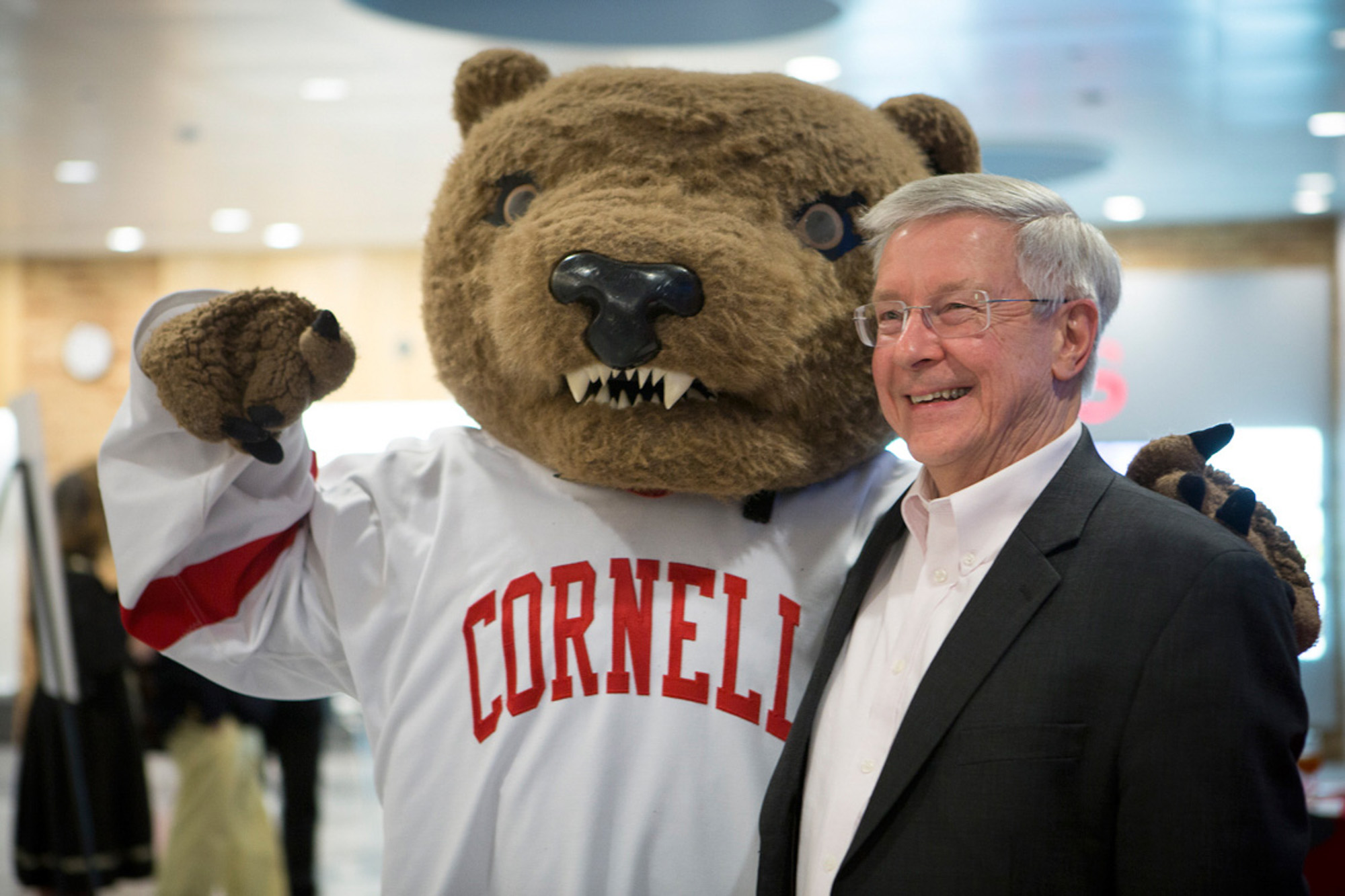 The Big Red Bear mascot stands side by side with a man in a dark blazer and white shirt.