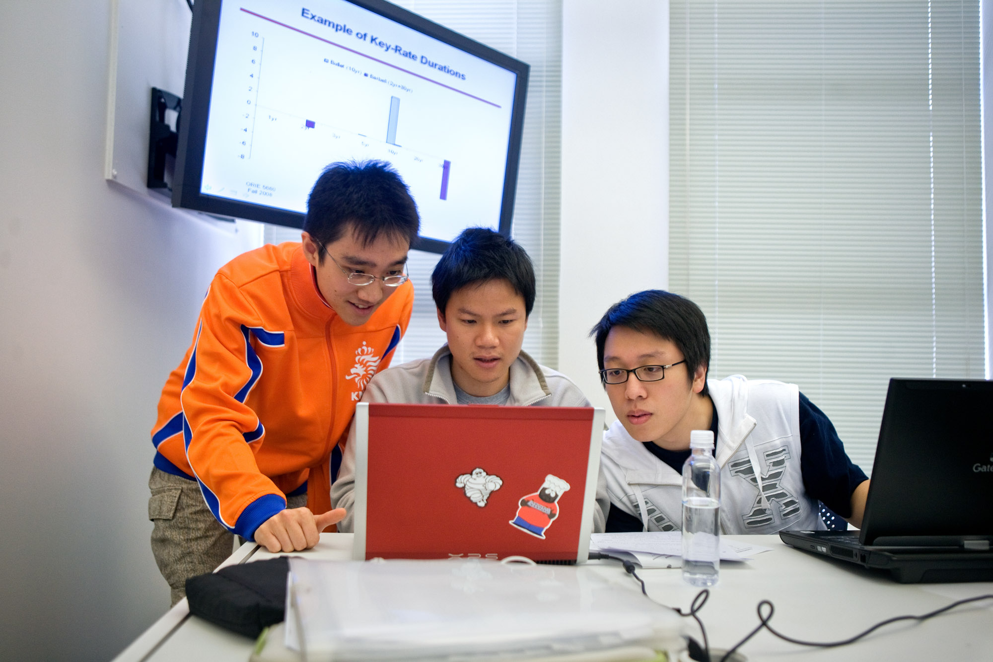 Three students look at an open laptop computer whose screen is not visible.