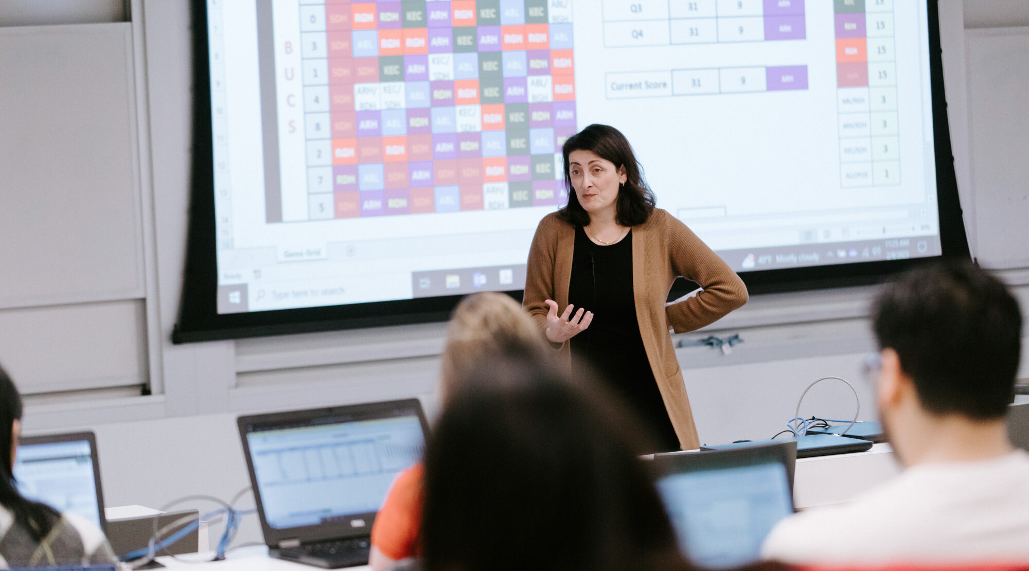 ORIE Professor Kathryn Caggiano lectures a class while standing in front of a screen showing a colorful chart with data.