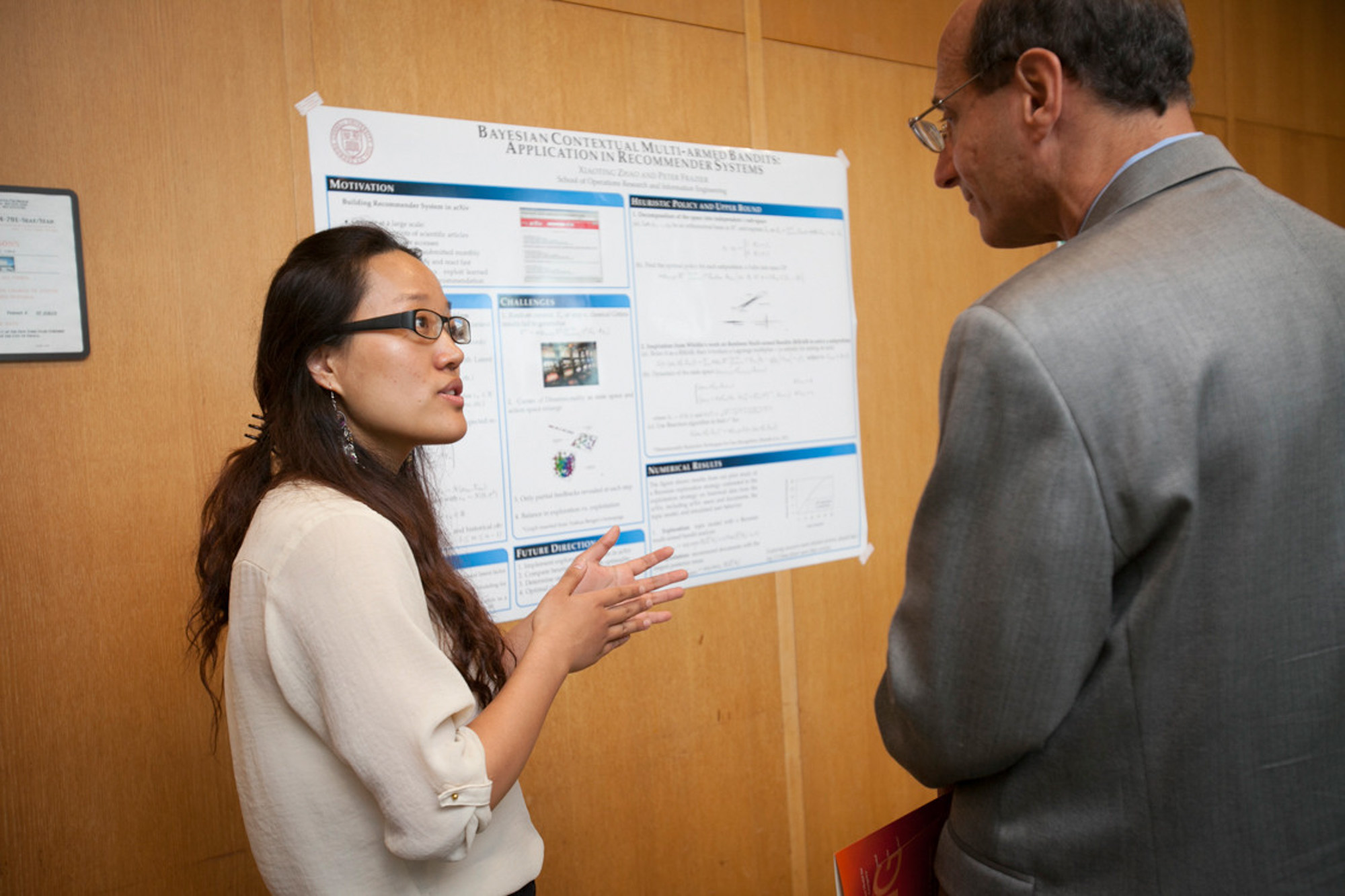 A student gestures while talking to a person looking at an academic poster.