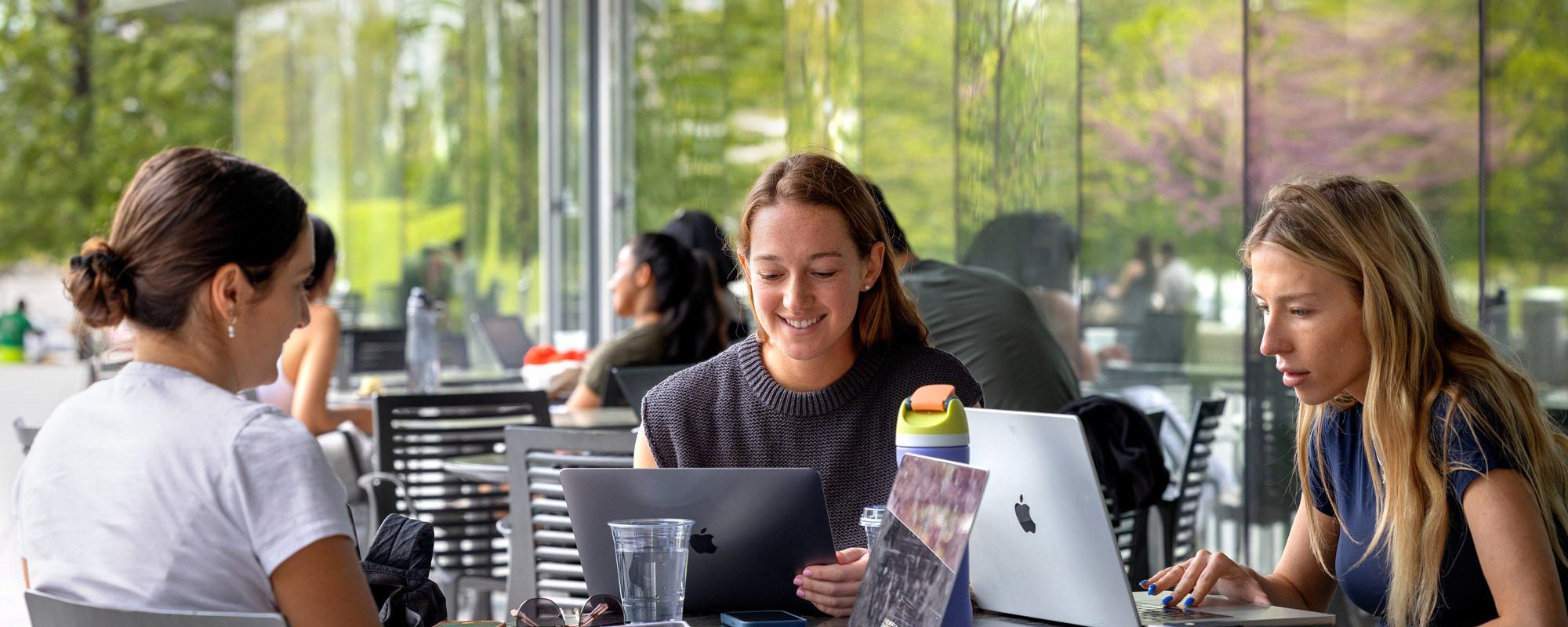 Group of 3 female students working together around a table outside