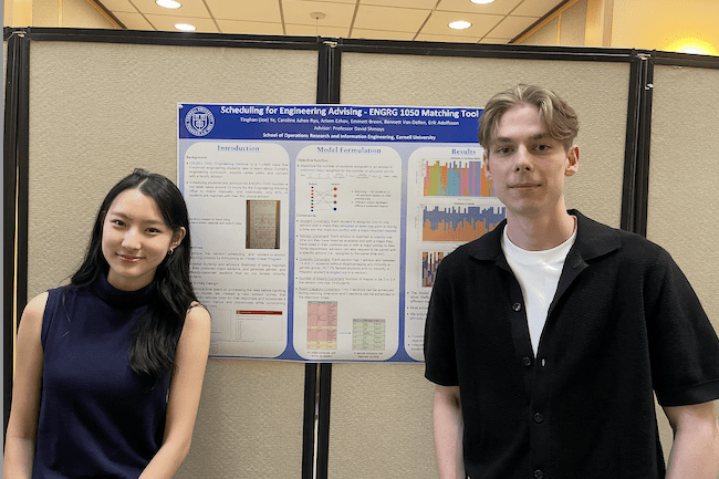Two undergraduate students stand in front of a research poster.