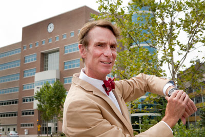 Bill Nye pointing to his watch in front of Rhodes Hall Clock