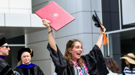 student joyfully holds graduation diploma and cap in hand