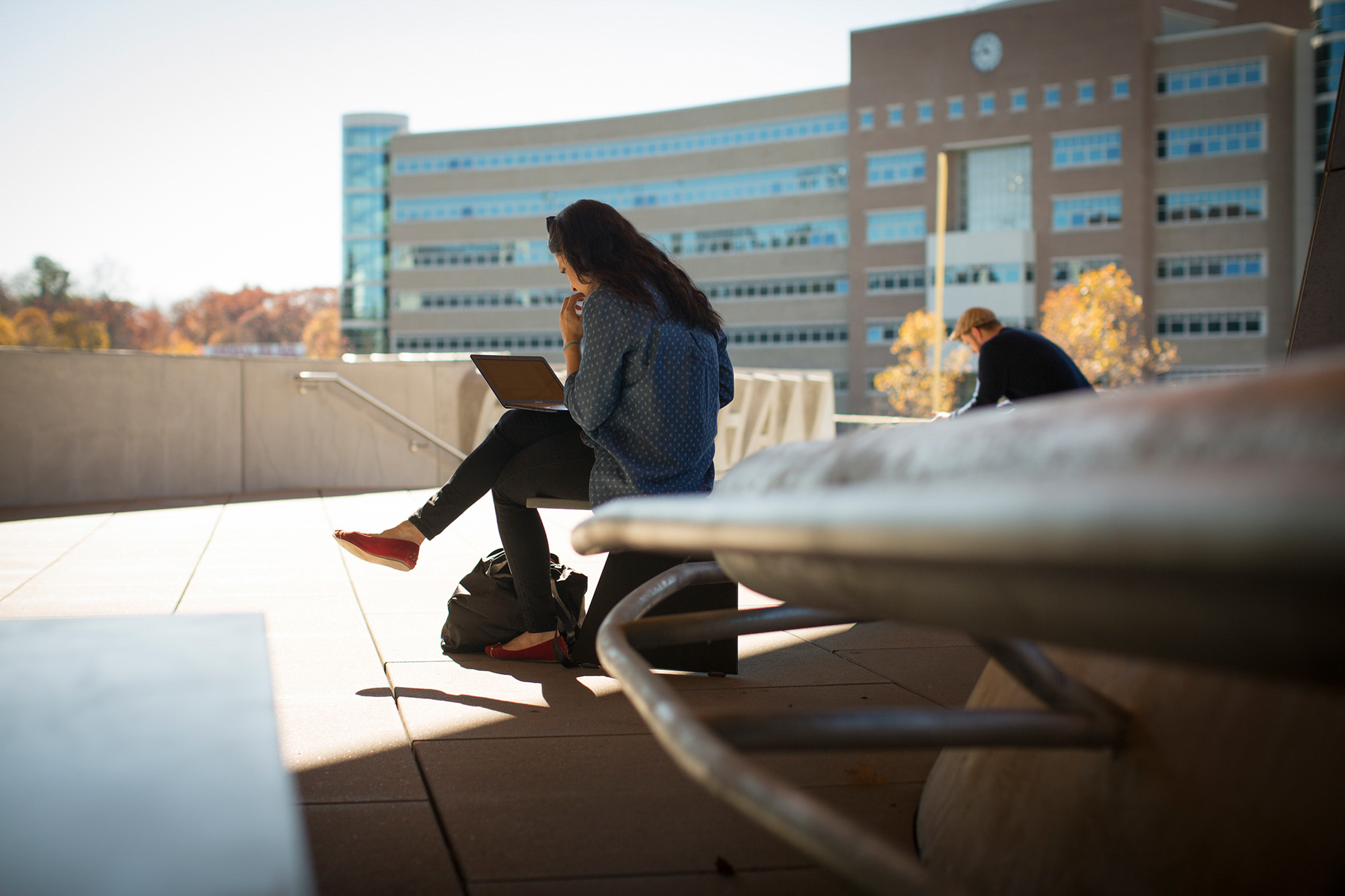 Two students study outside Gates Hall in fall with Rhodes Hall in the background.