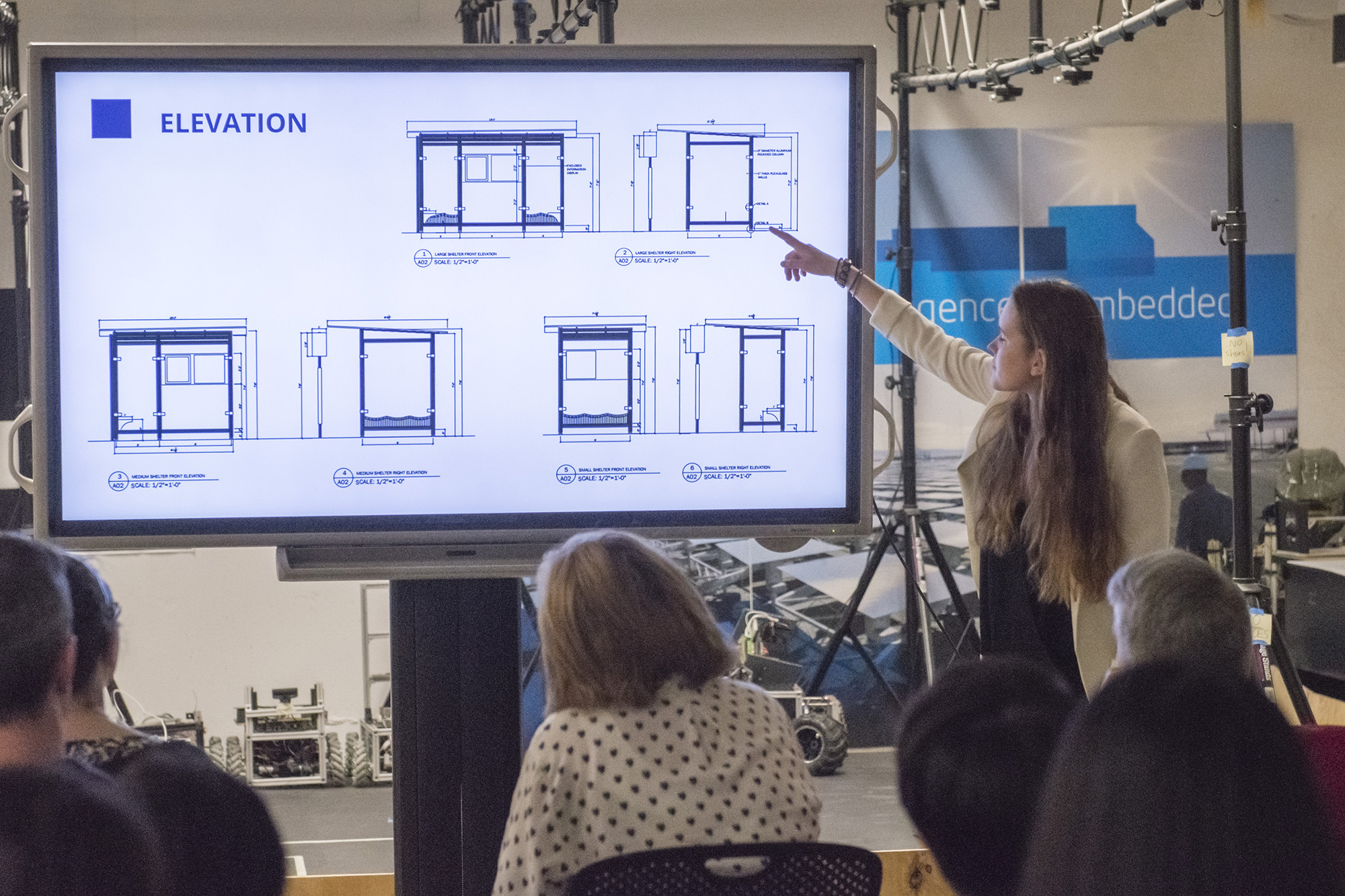 Woman standing in front of a screen, presenting to an audience.